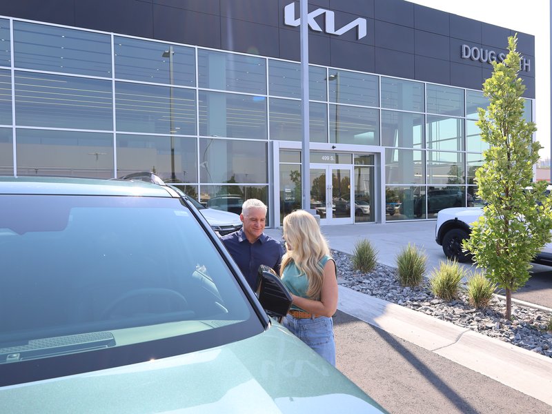 Two customers looking at a Kia parked outside the showroom entrance