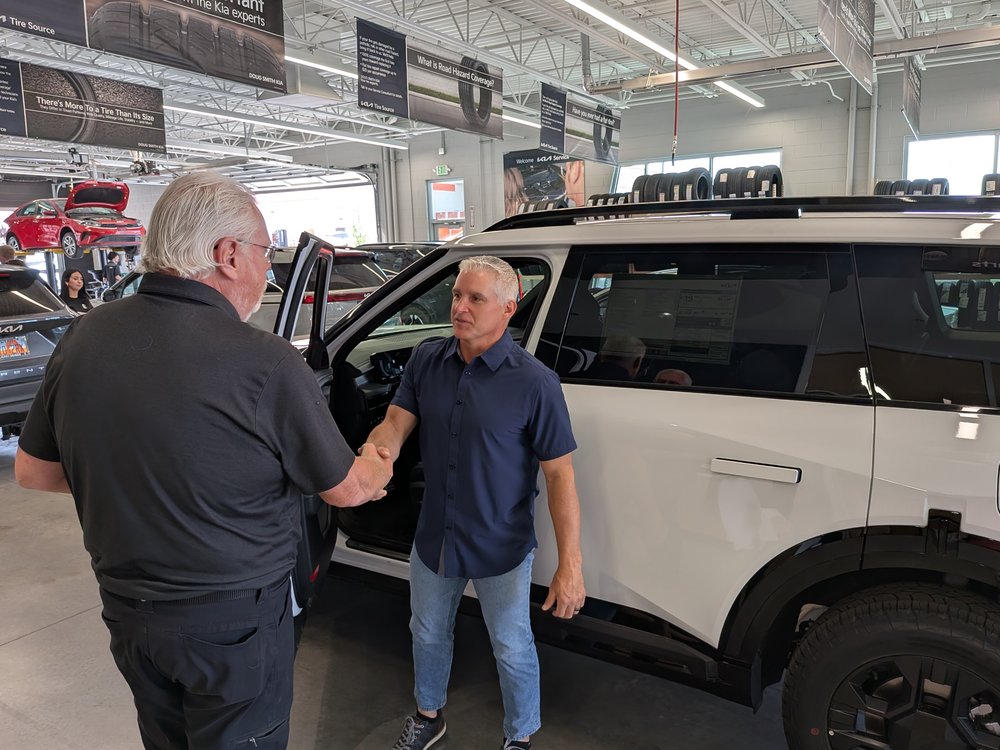 A Doug Smith Kia team member shaking hands with a customer beside a vehicle