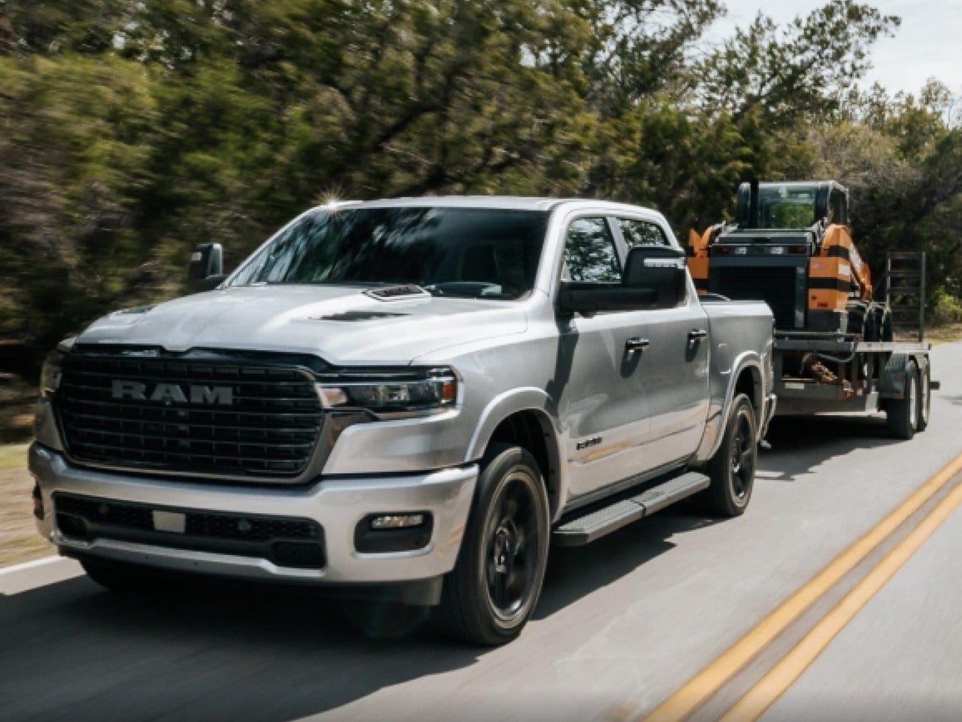 A silver Ram 1500 towing a skid steer on an equipment trailer