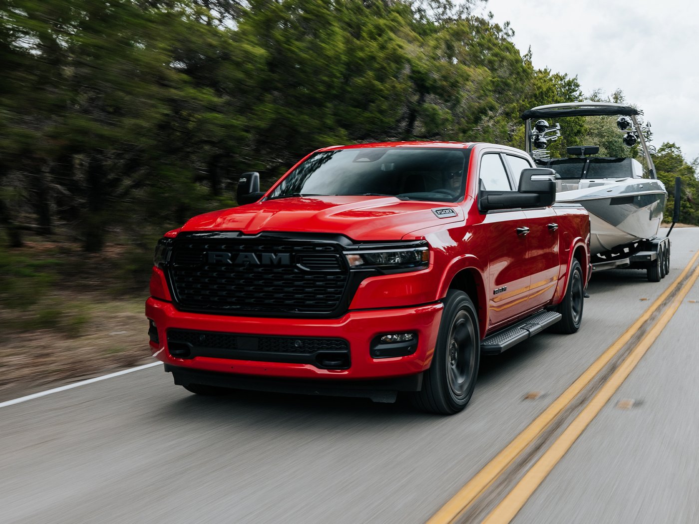 A red 2027 Ram 1500 towing a boat on a two-lane road