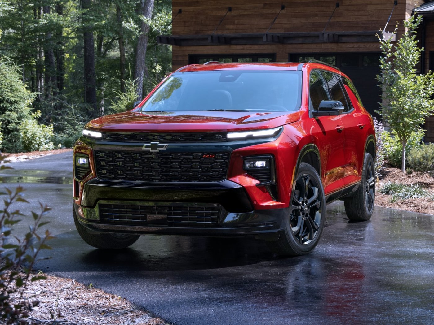 A red Traverse RS with black wheels and grille on a wet driveway in front of a wooded cabin