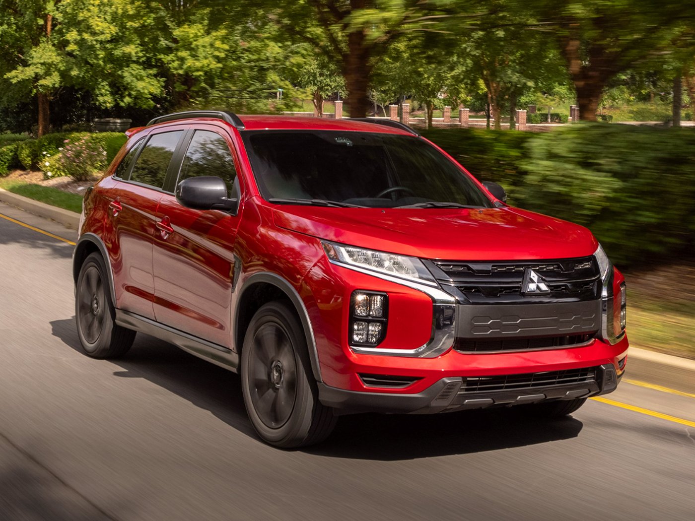 A red Mitsubishi Outlander Sport with black wheels driving on a tree-lined road