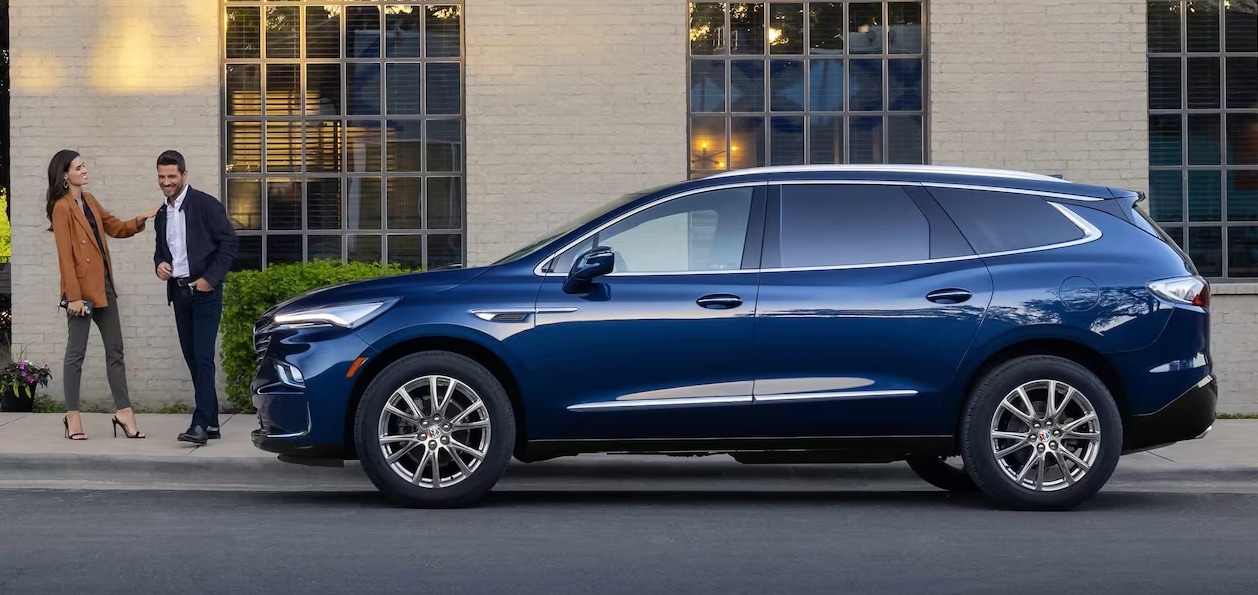 Blue 2024 Buick Enclave parked on street with man and woman standing nearby