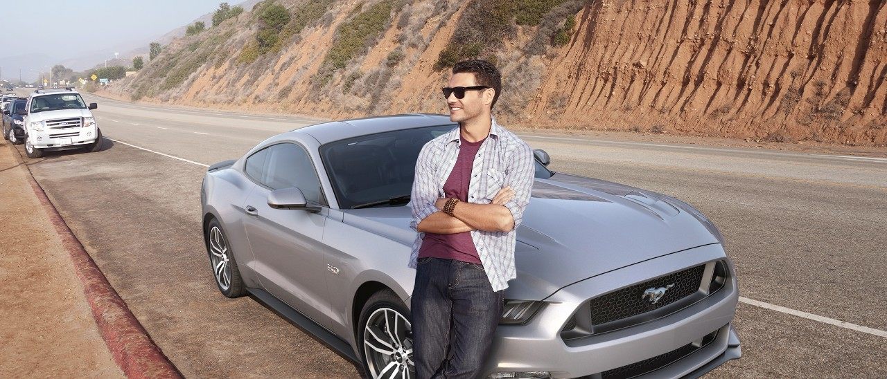 man leans against past model Ford Mustang
