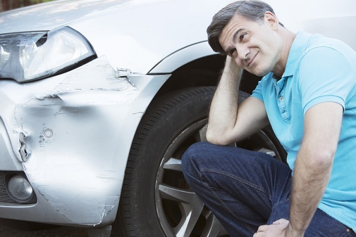Man upset next to a badly dented fender