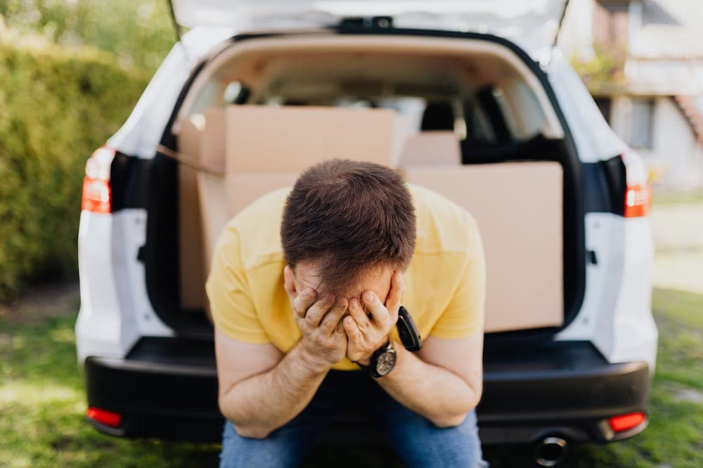 man with head in hands sitting on car