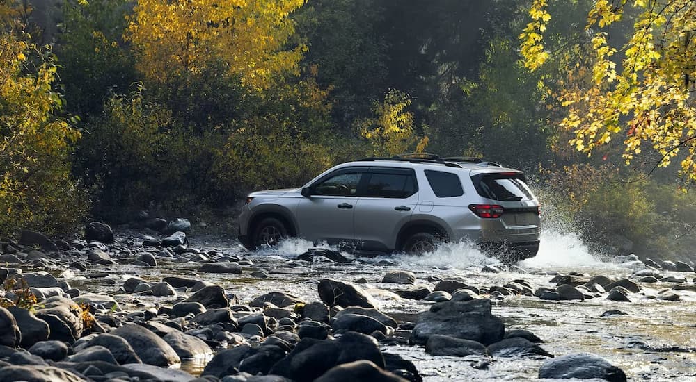A grey 2024 Honda Pilot is shown from the side driving through a river.