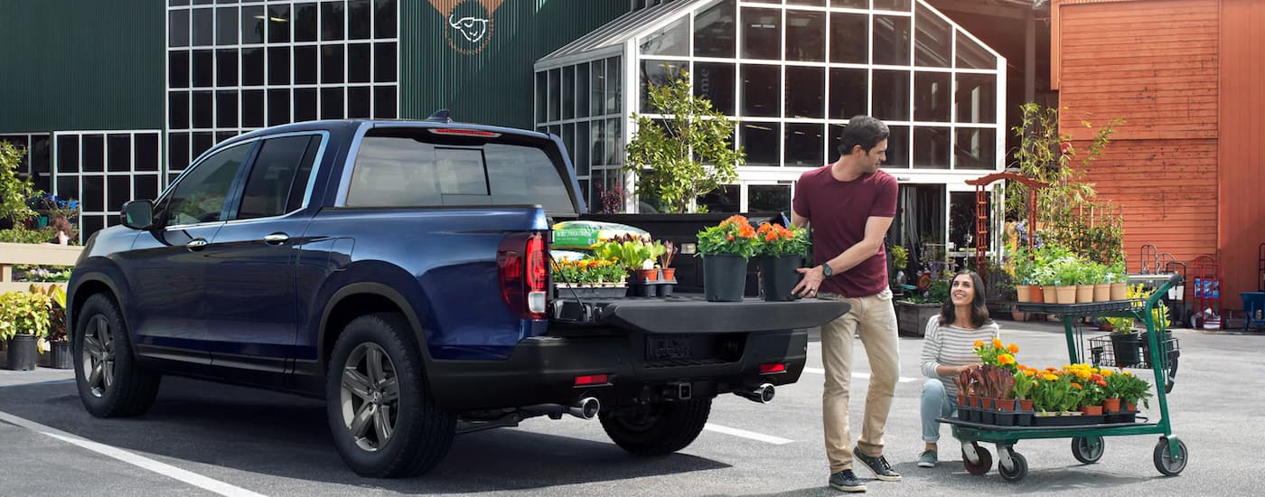 A man is shown putting flowers in the bed of a blue 2023 Honda Ridgeline.