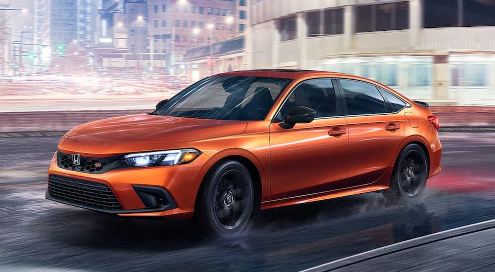 An orange 2022 Honda Civic Si is shown driving on a city highway after a rainstorm.