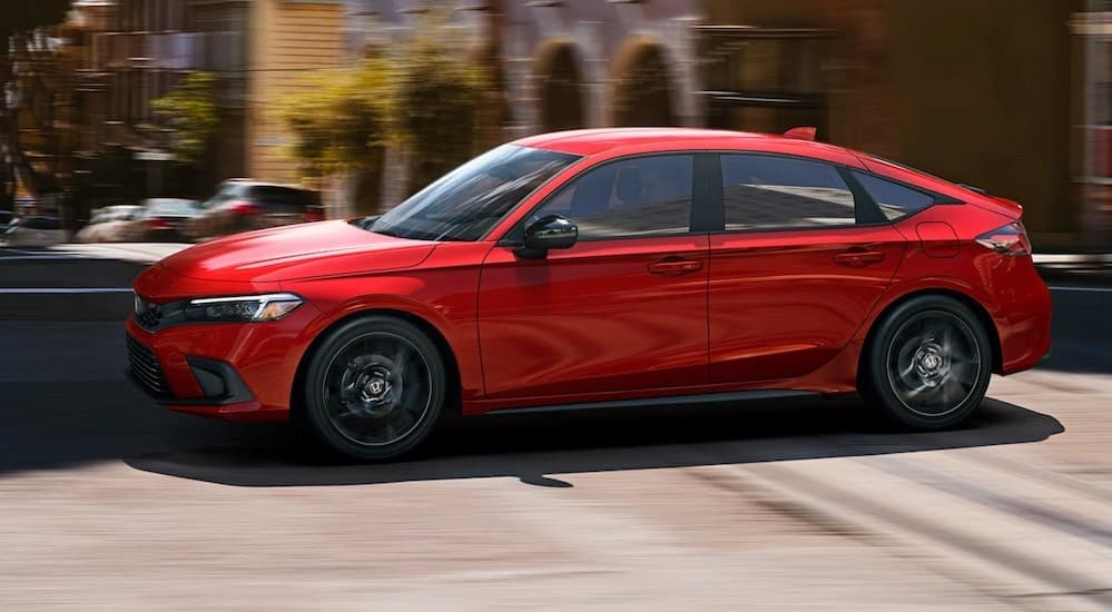 A red 2024 Honda Civic Hatchback is shown driving near city buildings.
