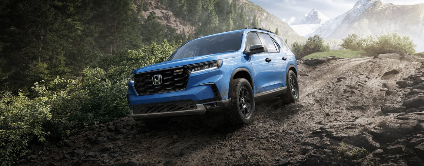A blue 2023 Honda Pilot Trailsport is shown off-roading on a muddy path.