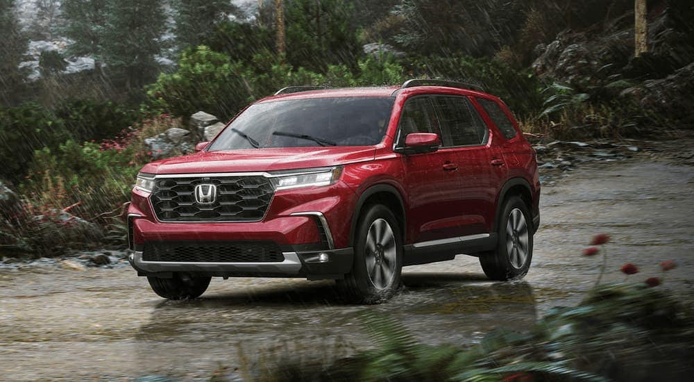 A red 2023 Honda Pilot Elite is shown driving on a road while it's raining.