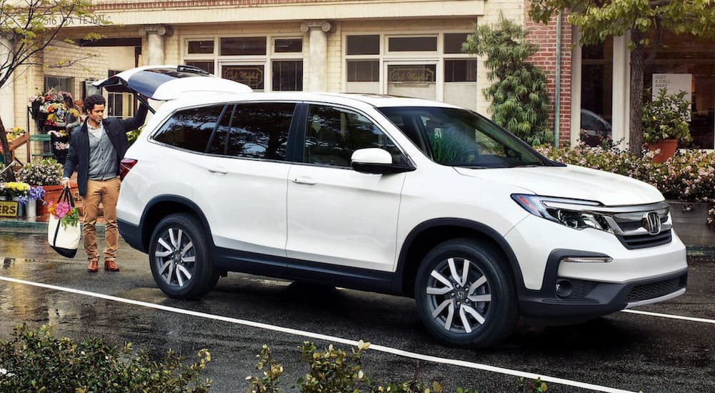A white 2022 Honda Pilot is shown being loaded with groceries in a parking lot outside of a store.