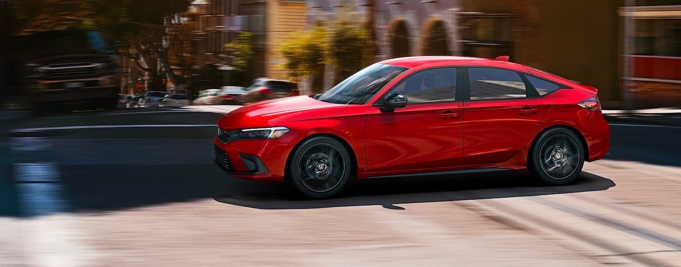 A red 2023 Honda Civic Sport is shown from the side driving on a city street.