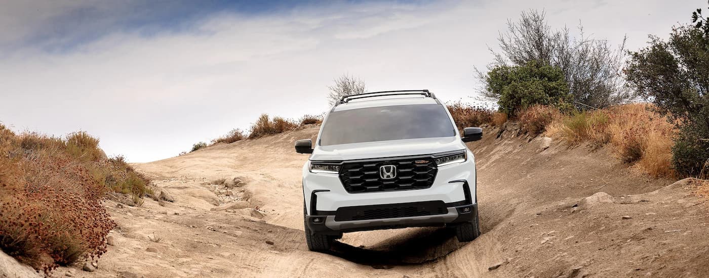 A white 2023 Honda Pilot Trailsport is shown from the front driving on a dirt trail.