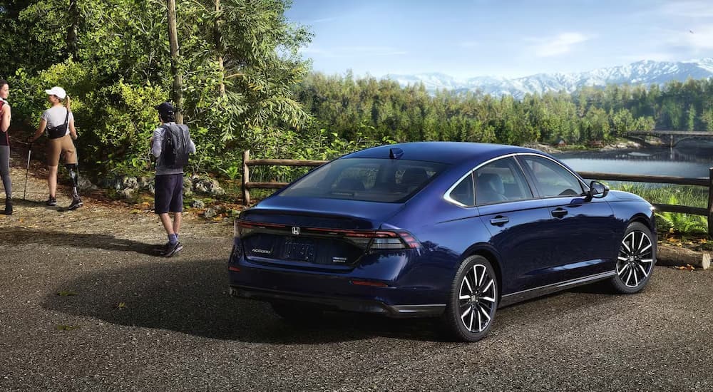 A blue 2023 Honda Accord Touring Hybrid for sale is shown from a rear angle parked near a hiking trail entrance.