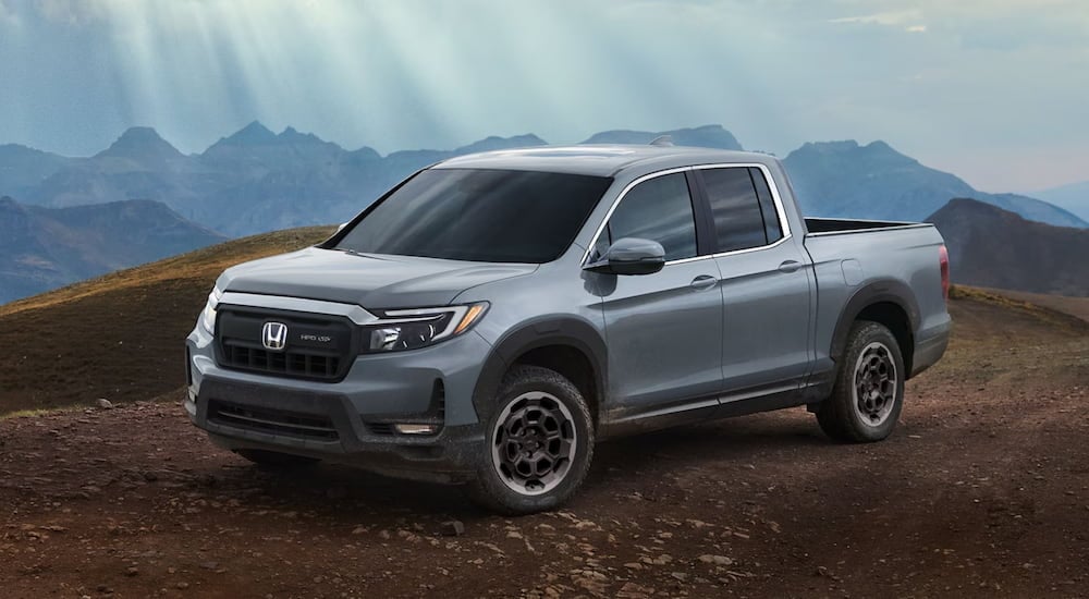 A new Honda Ridgeline for sale, a grey 2024 Honda Ridgeline RTL, is shown parked in a large open dirt area.
