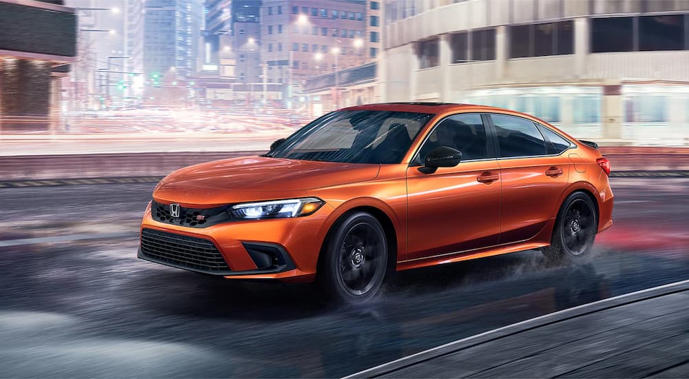 An orange 2022 Honda Civic Si is shown driving on a city street at night.