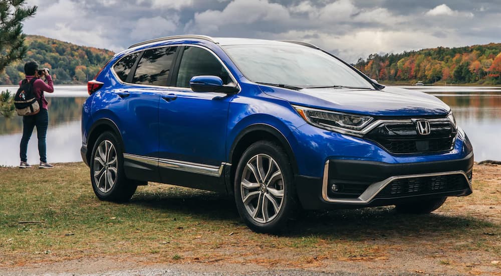 A popular used suv for sale, a blue 2021 Honda CR-V Elite, is shown parked at a lake.