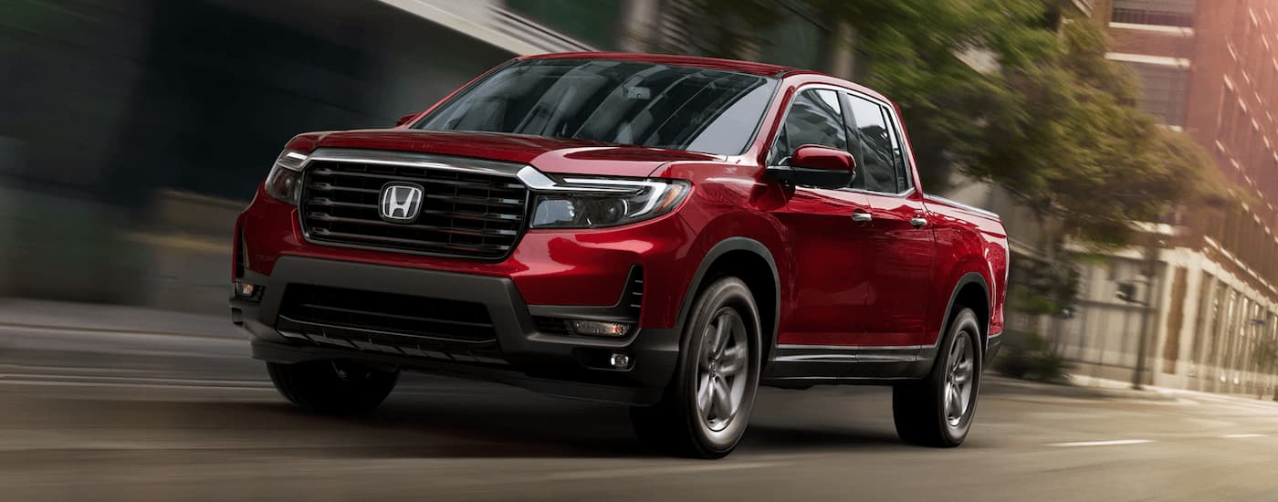 A red 2023 Honda Ridgeline RTL-E is shown driving on a city street after leaving a Honda dealer near Claiborne, LA.