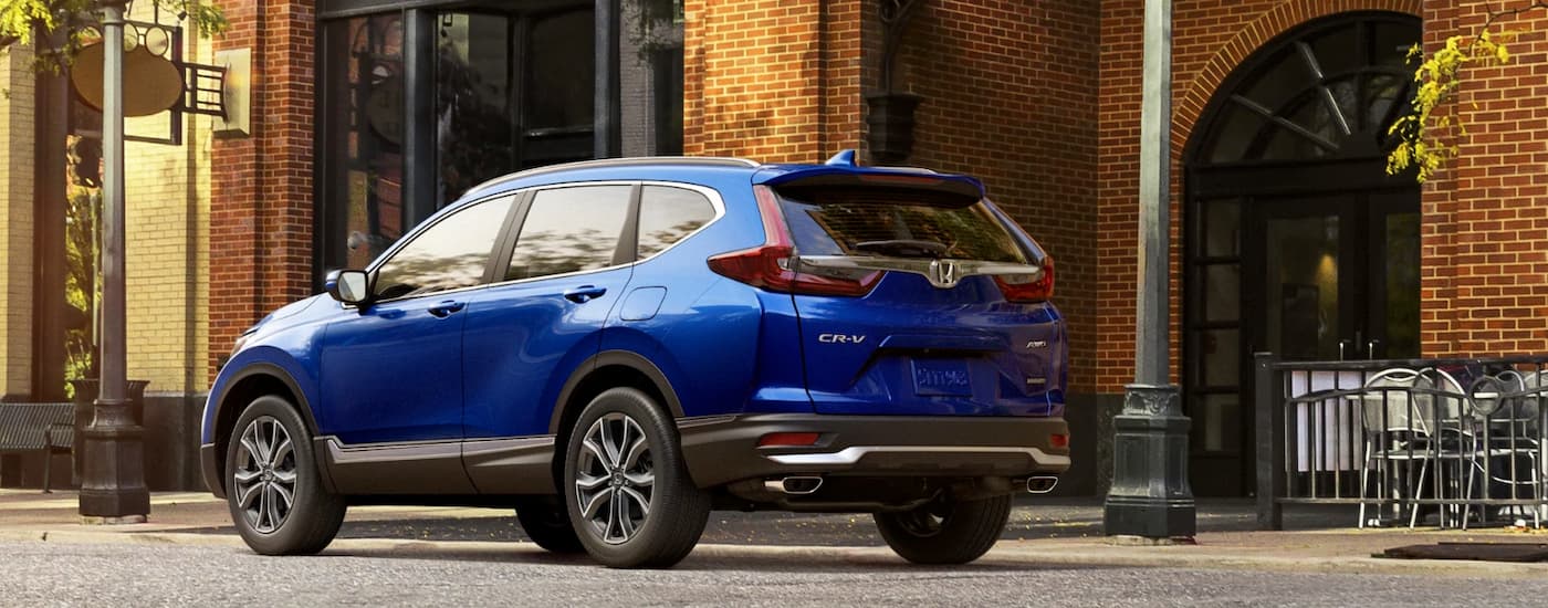 A blue 2022 Honda CR-V Hybrid is shown from the rear parked on the side of city street.
