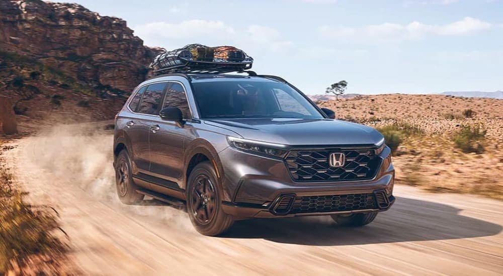 A grey 2024 Honda CR-V Sport Hybrid driving down a dusty trail.
