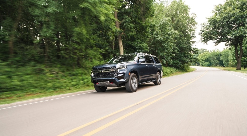 A grey  2021 Chevy Suburban Z71 is shown driving on a tree-lined road.