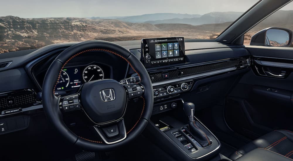 The steering wheel and black dashboard in the interior of a 2024 Honda CR-V Sport Touring.