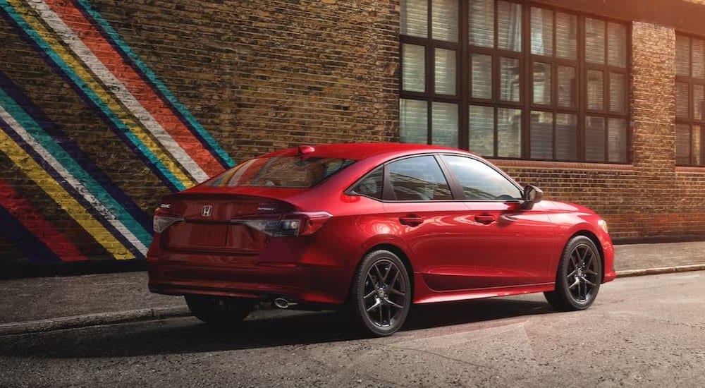 Rear view of a red 2023 Honda Civic Sport sedan parked near a brick wall.
