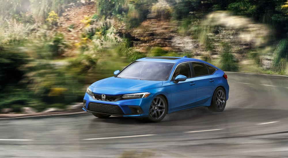 A blue 2023 Honda Civic Hatchback Sport Touring driving on a rainy road.