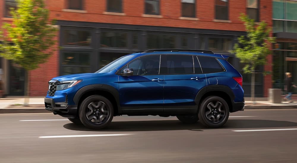 A blue 2022 Honda Passport Elite is shown driving on a city street after visiting a used auto dealer.