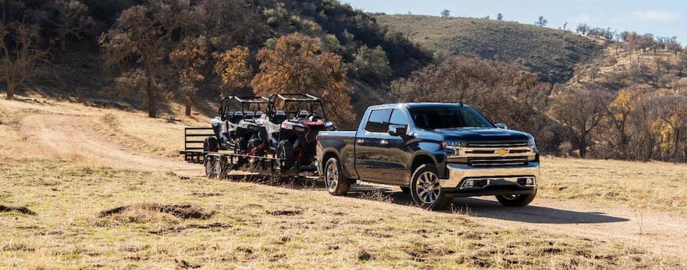 A black 2020 Chevy Silverado 1500 is towing a trailer in a field.