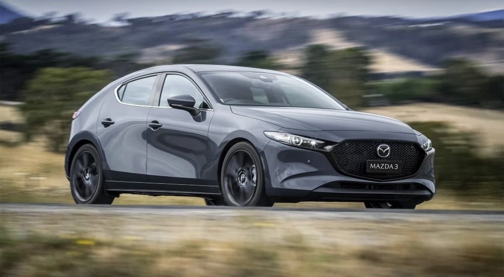 A gray 2023 Mazda3 is shown driving on a road.