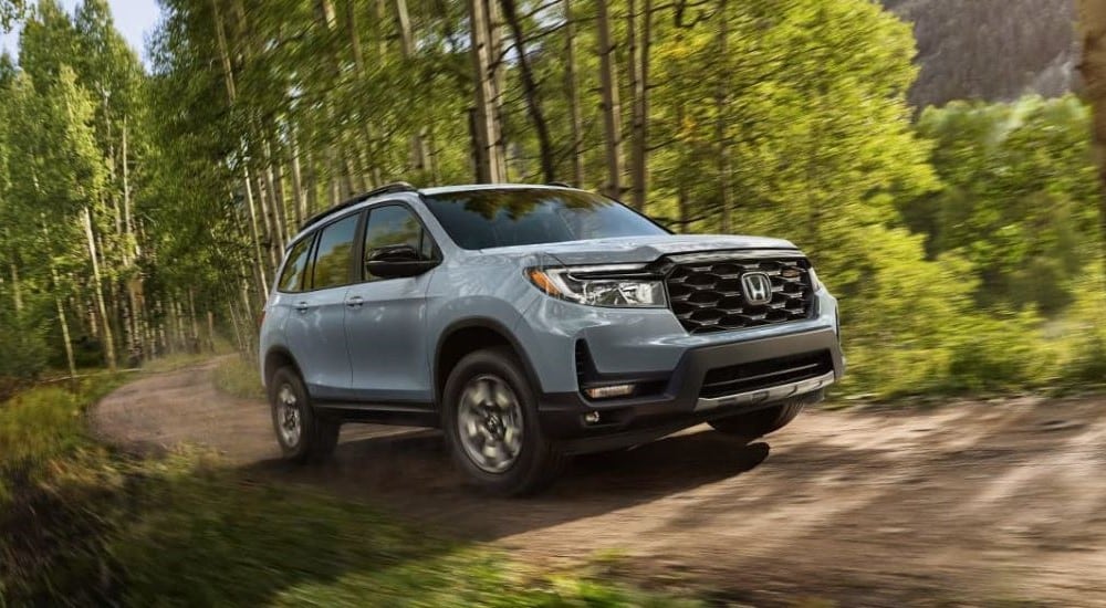 One of the most popular Honda SUVs for sale, a silver 2023 Honda Passport TrailSport, is shown on a tree-lined path.