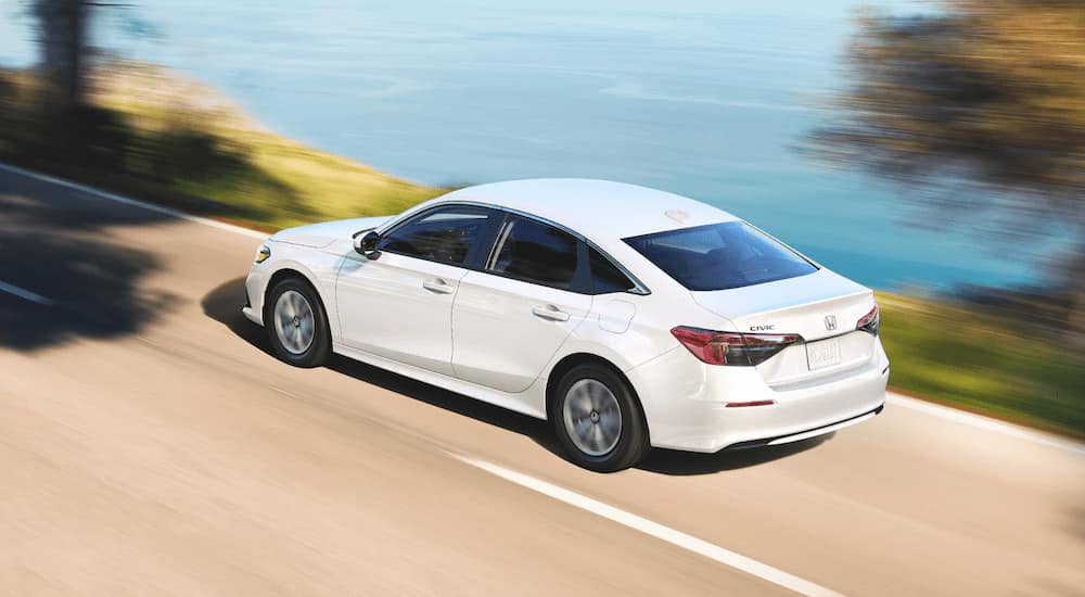 A white 2022 Honda Civic is shown from a rear angle while driving on an open road.