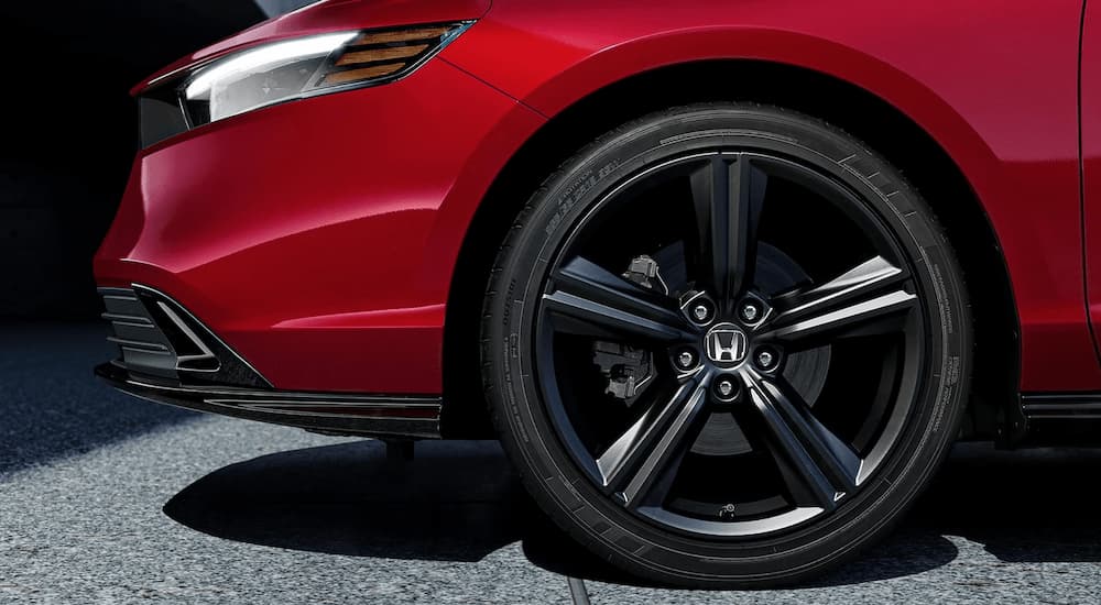 The front headlight and tire on a red 2023 Honda Accord Sport Hybrid are shown from the side.