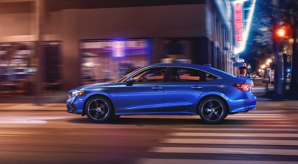 A blue 2024 Honda Civic for sale is shown driving on a city street.