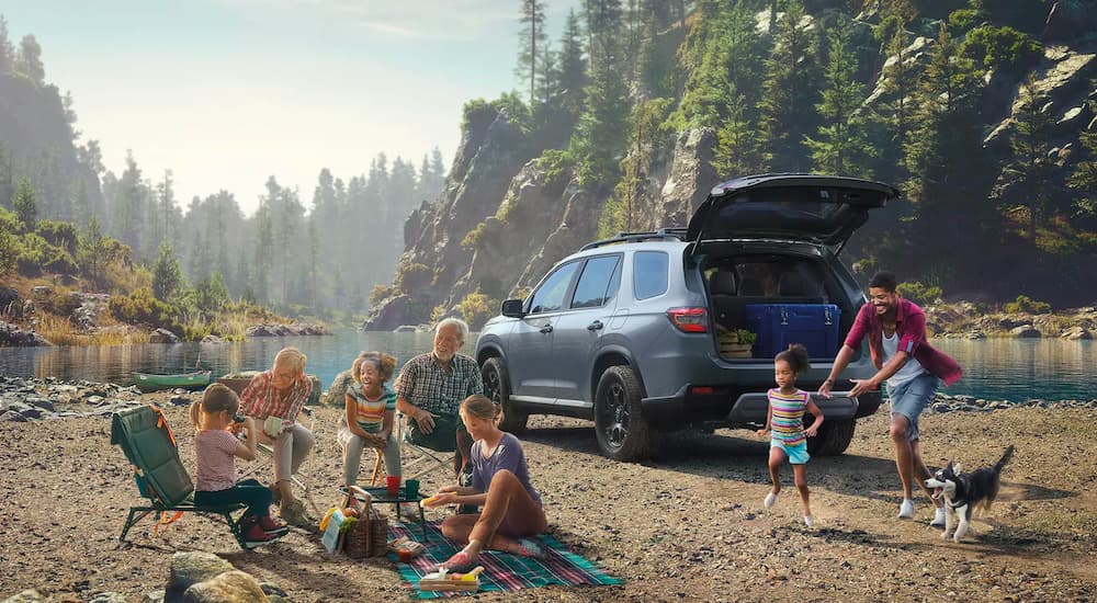 A grey 2023 Honda Pilot Trailsport is shown near a pond and a family.