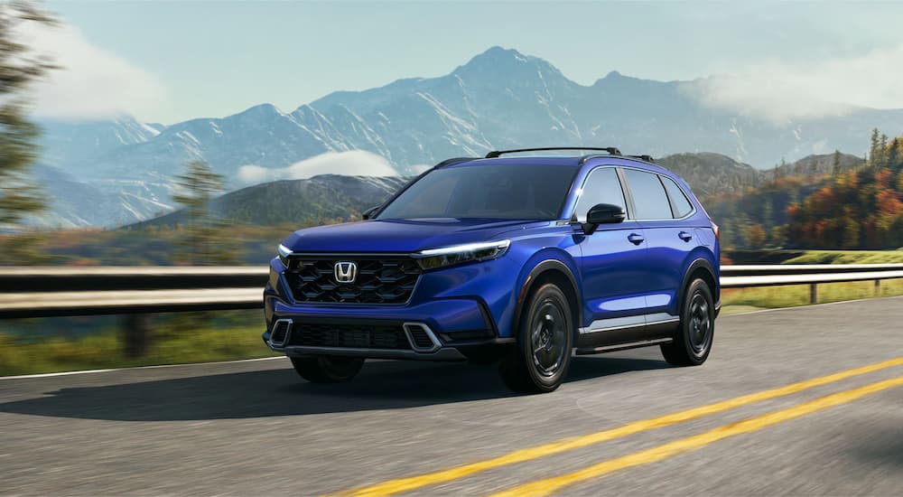 A blue 2023 Honda CR-V Sport Touring is shown from a side angle while driving on a road through the mountains.