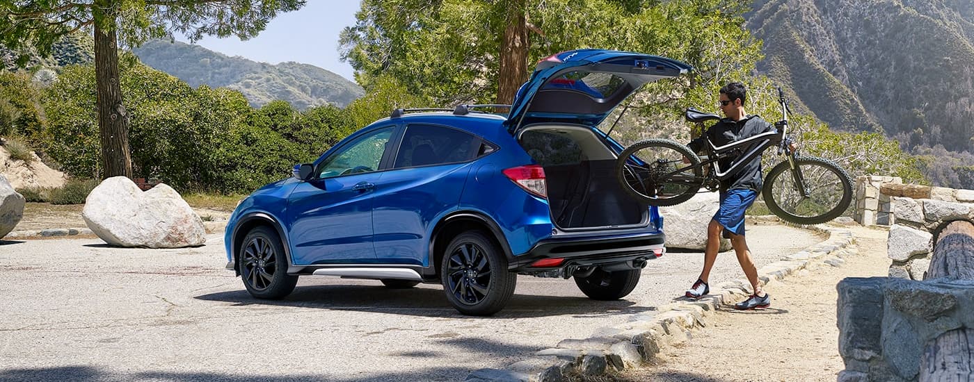 A person is shown loading a bike into the trunk of a blue 2021 Honda HR-V Sport.