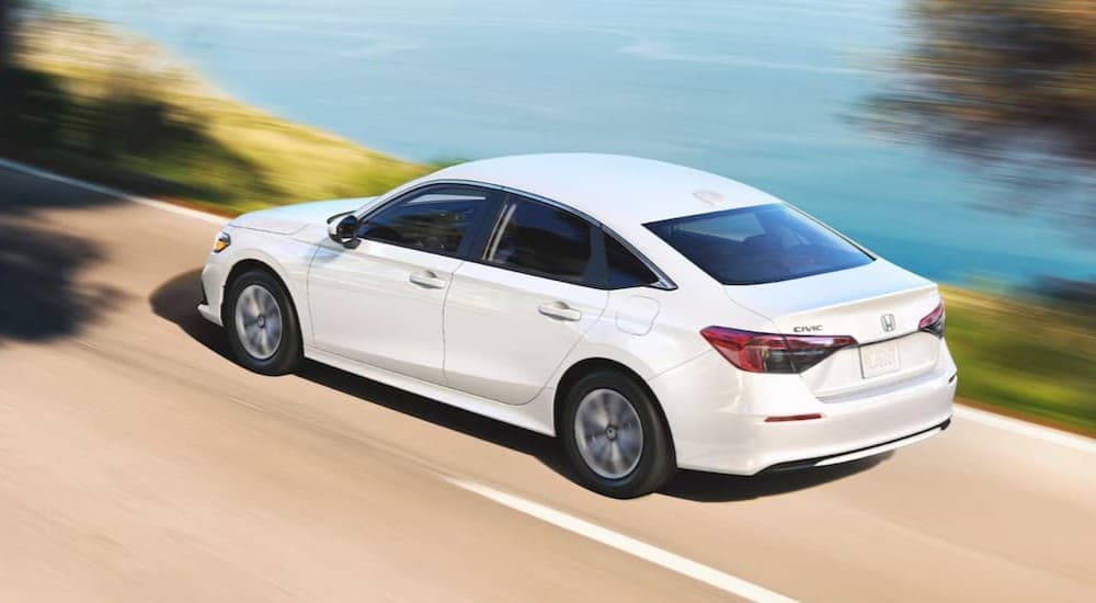 A white 2024 Honda Civic sedan is shown driving near an ocean.