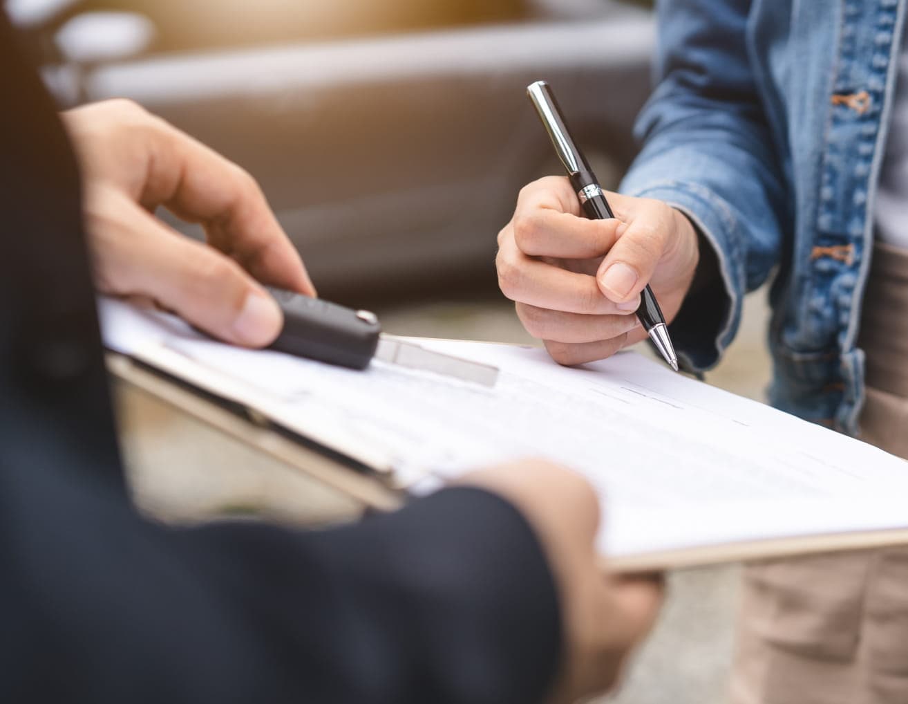 Customer signing paperwork while receiving a car key at a dealership.