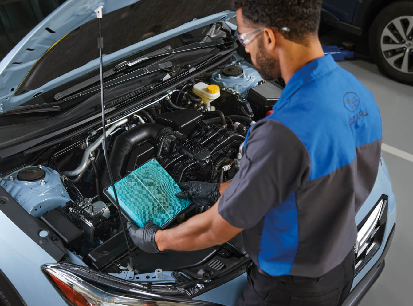 An overhead shot of a certified Subaru service technician inspecting and replacing an engine air filter under the hood of a 2026 Subaru Impreza.