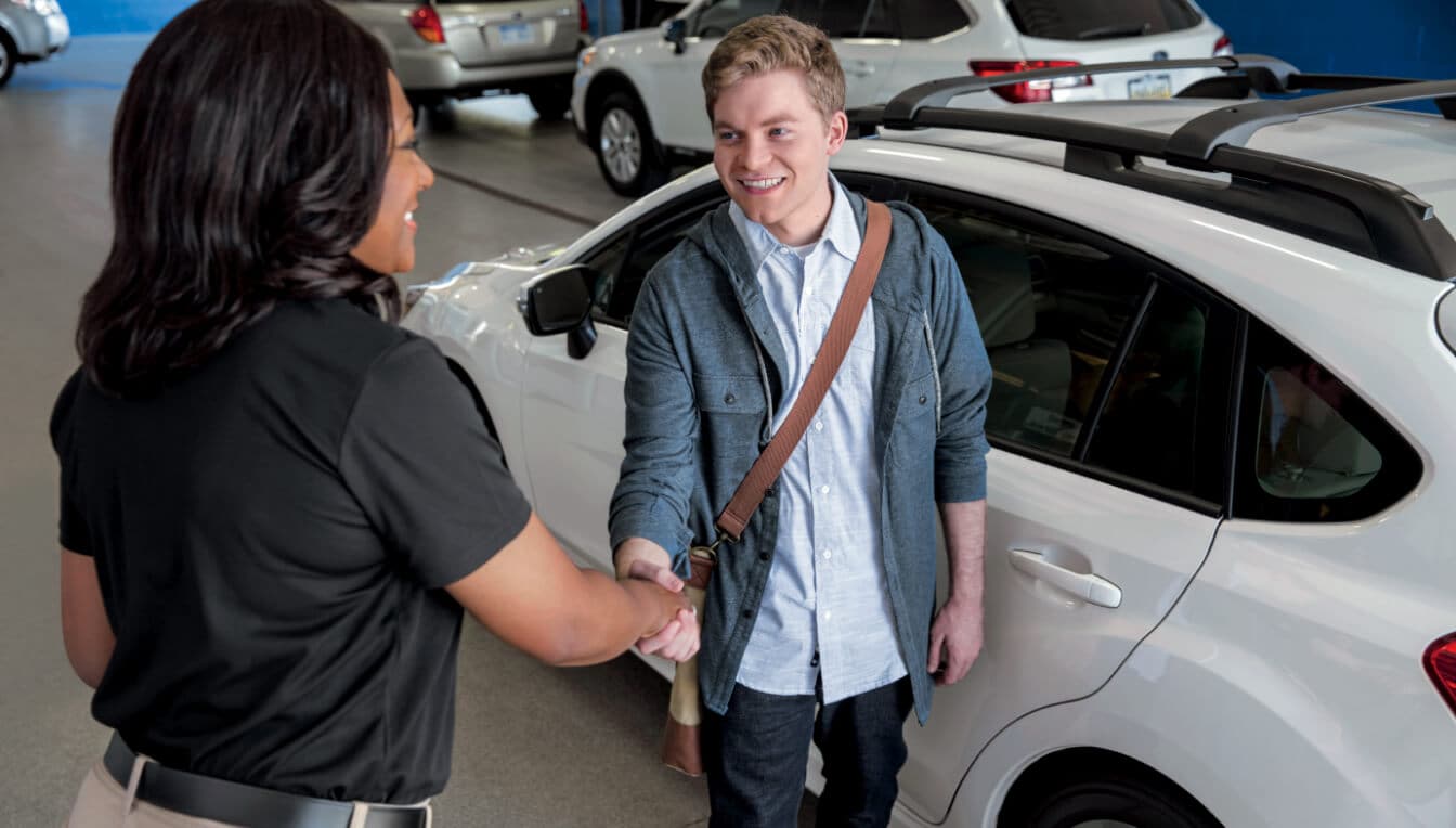 A Subaru service advisor shaking hands with a customer next to a 2026 Subaru Crosstrek inside a dealership service.