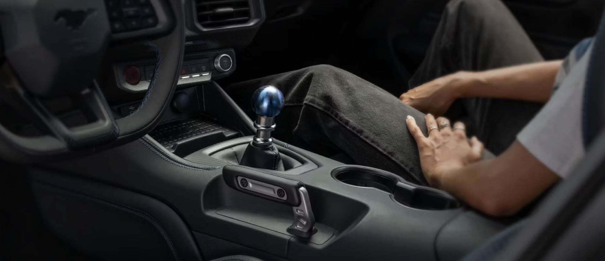 Close-up of a Ford Mustang interior showing the center console with a blue manual shift knob