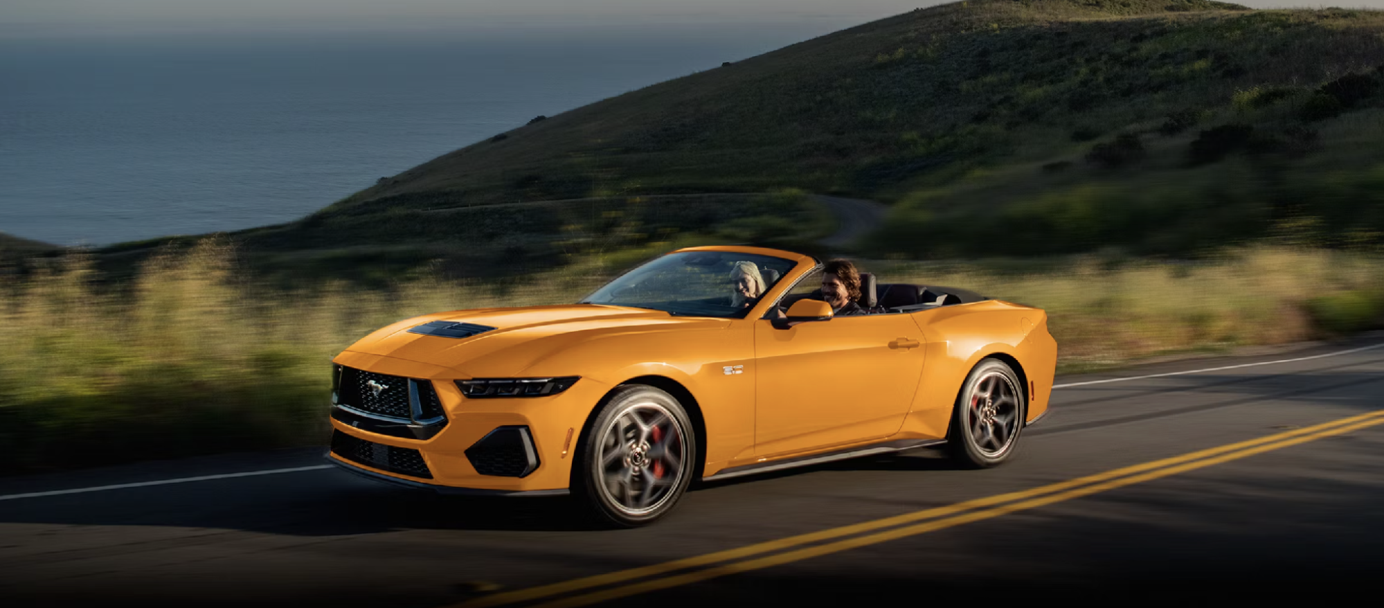 Ford Mustang GT convertible with the top down driving along a coastal road