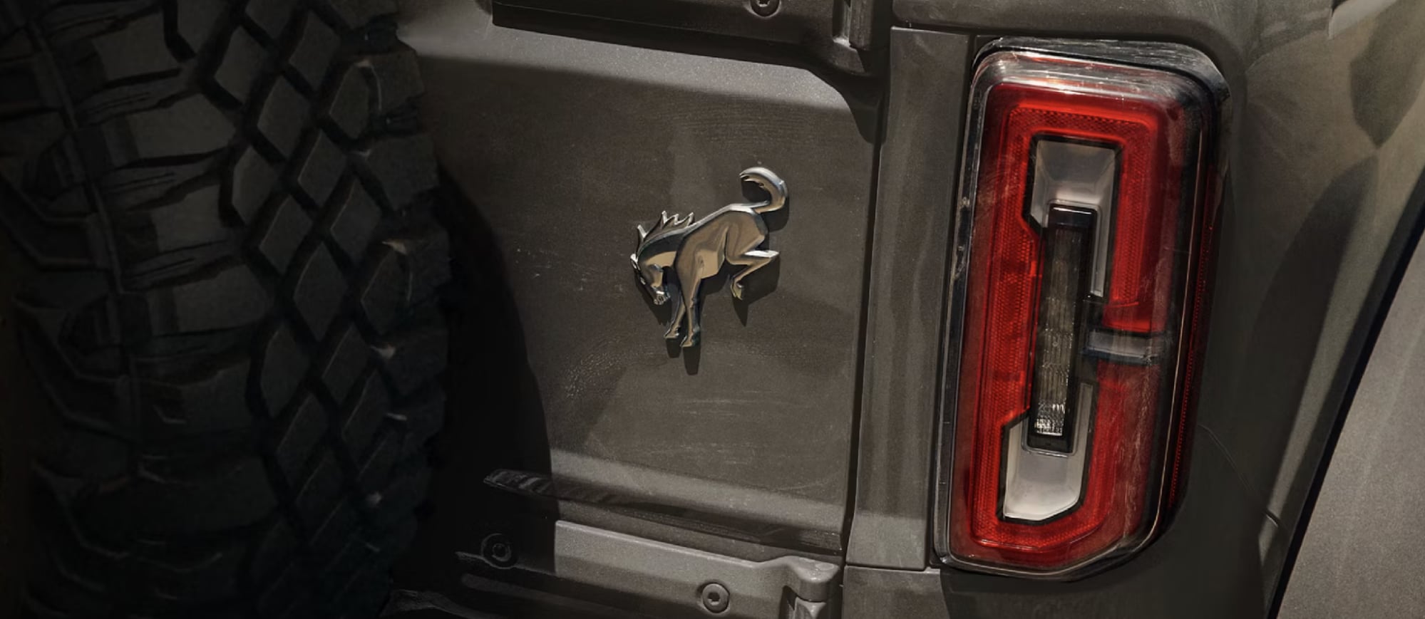 Close-up of a Ford Bronco rear quarter panel showing the chrome Bronco emblem, taillight, and rugged off-road tire.