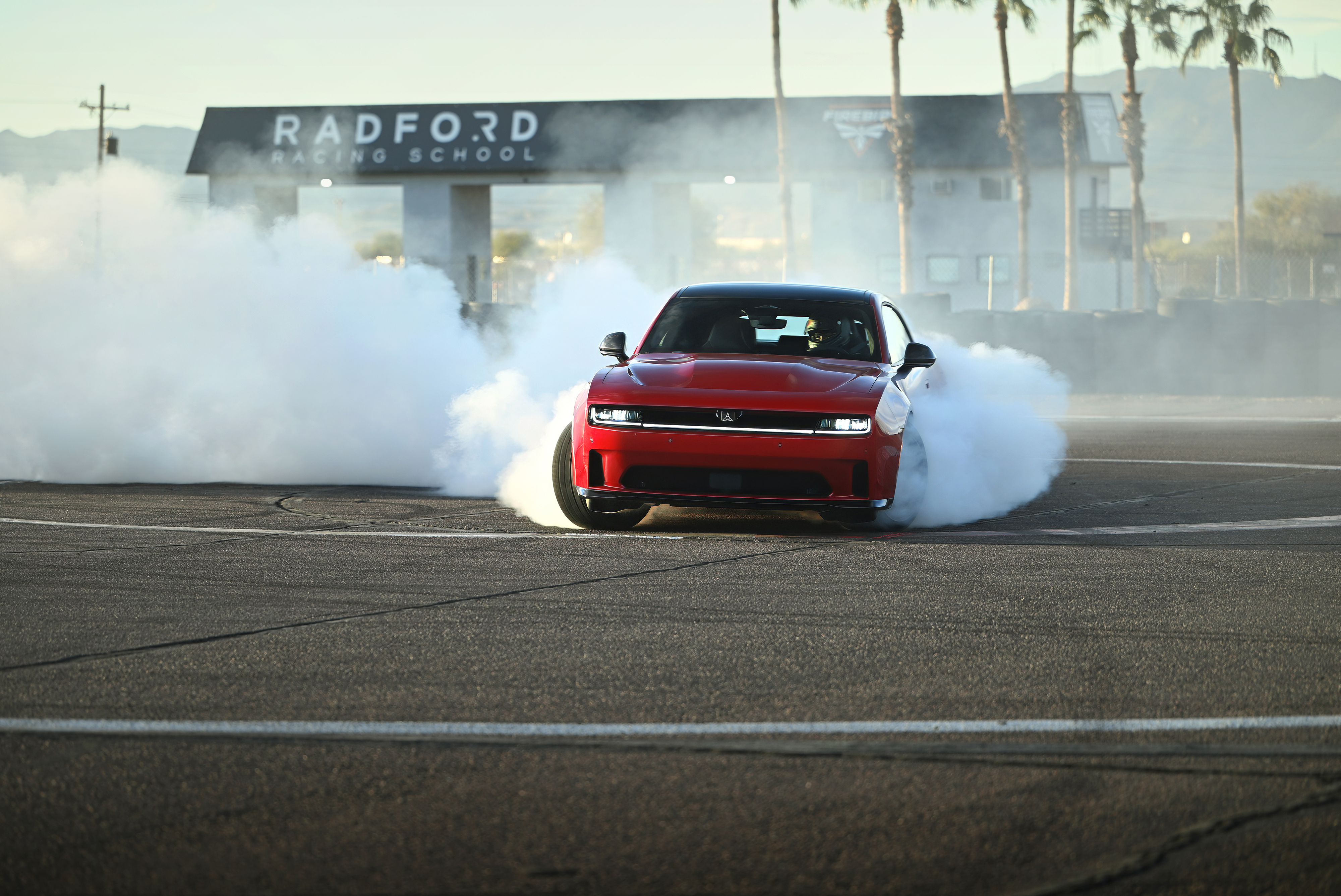 Red Dodge Charger doing a burnout at a racetrack