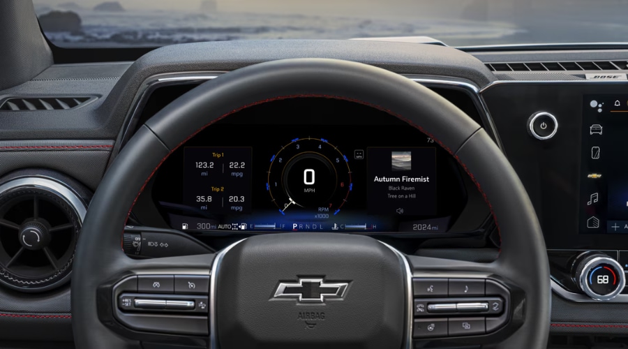 A driver's view of the 2026 Chevy Colorado interior, showing the leather-wrapped steering wheel with red stitching and the digital driver cluster displaying real-world MPG, evaluated in our 2026 Chevy Colorado Highway Review in Marlton, NJ.