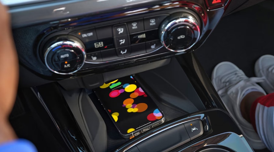 Close-up interior detail of the 2026 Chevy Trax center console featuring an available wireless charging pad with a smartphone powering up, highlighting convenient tech amenities for South Jersey commuters near Marlton, Cherry Hill, and Evesham.